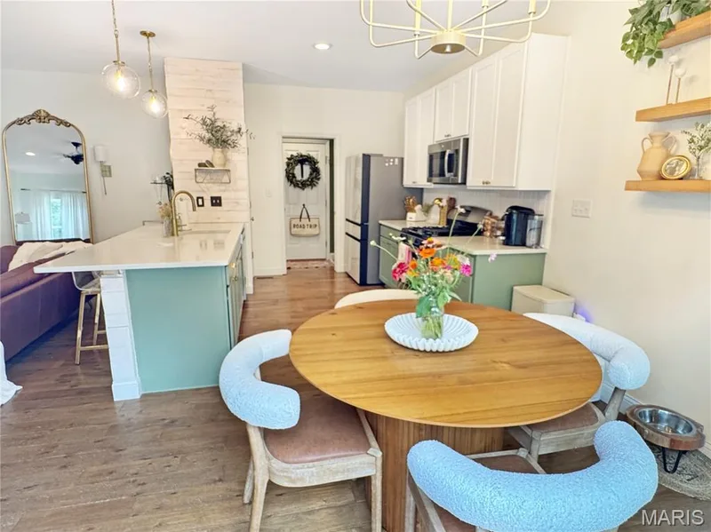 Kitchen featuring wood-finish flooring, white cabinetry, integrated stainless steel appliances, and a central island with a light-toned countertop — 4024 Glengarry Drive, Wentzville, MO 63385