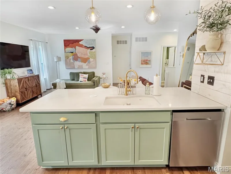 Kitchen island with light green cabinetry, white countertop, and an undermount sink with a gold-finish faucet — 4024 Glengarry Drive, Wentzville, MO 63385