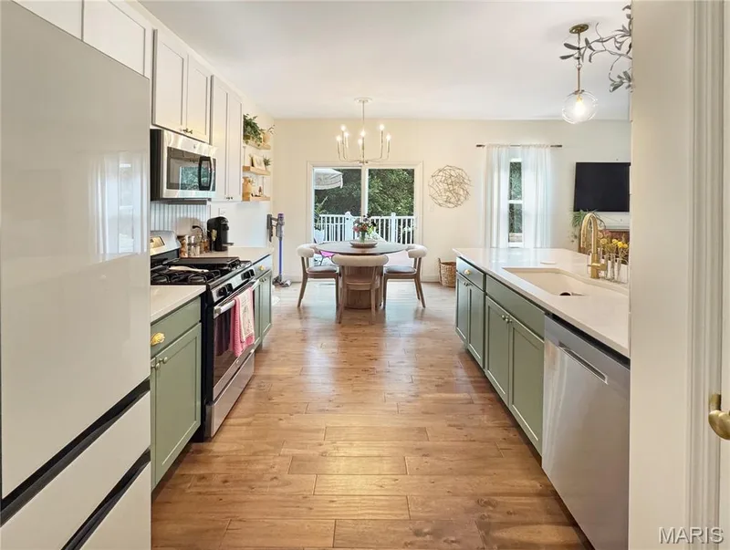 Modern kitchen featuring wood-finish flooring, two-tone cabinetry with upper white and lower sage-green finishes, stainless steel appliances, and light-toned countertops — 4024 Glengarry Drive, Wentzville, MO 63385
