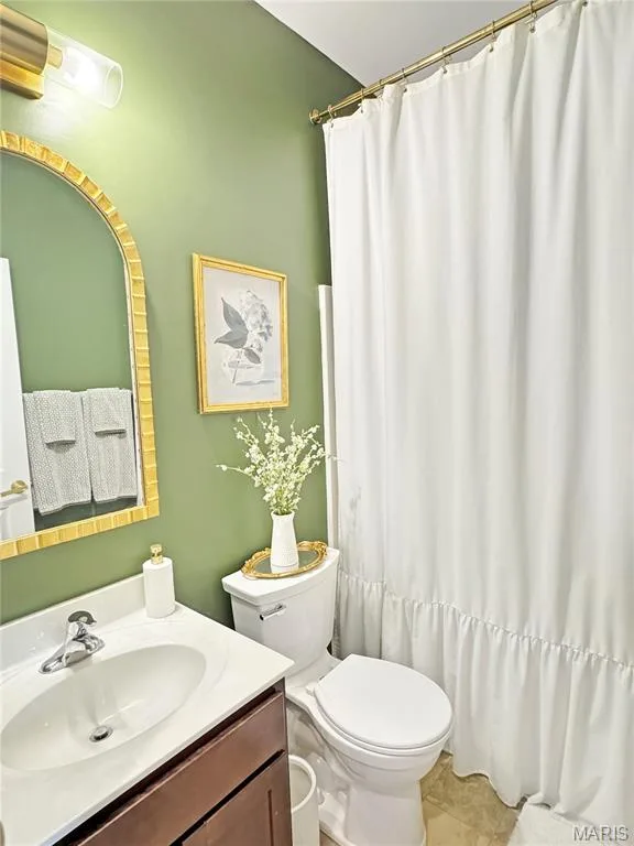 Bathroom featuring a wood-finish vanity with a white countertop, toilet, and shower curtain with a decorative rod — 4024 Glengarry Drive, Wentzville, MO 63385