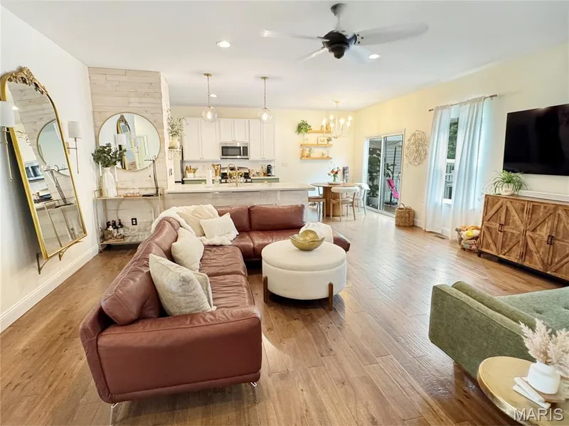 Open-concept living area featuring wood-finish flooring, a ceiling fan, and a kitchen with white cabinetry and pendant lighting — 4024 Glengarry Drive, Wentzville, MO 63385