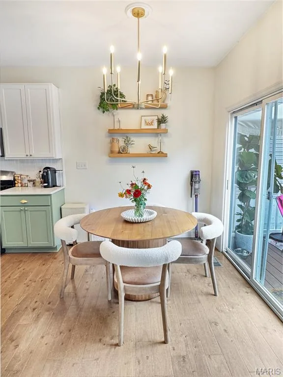 Bright dining area featuring a round wood-finish table, natural light from sliding glass doors, warm wood-finish flooring, and a brass multi-pendant chandelier with candle-style bulbs — 4024 Glengarry Drive, Wentzville, MO 63385