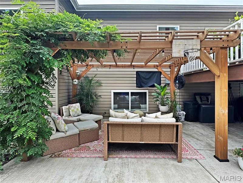 Expansive concrete patio with a wooden pergola, lush green foliage, and horizontal siding — 4024 Glengarry Drive, Wentzville, MO 63385