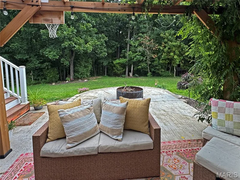 Backyard patio featuring a wood pergola, concrete hardscaping, wood steps with white railings, and a fire pit — 4024 Glengarry Drive, Wentzville, MO 63385