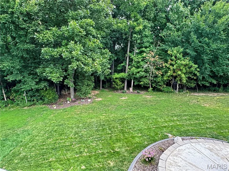 Expansive lawn surrounded by mature trees, featuring a curved paver patio with a decorative border — 4024 Glengarry Drive, Wentzville, MO 63385