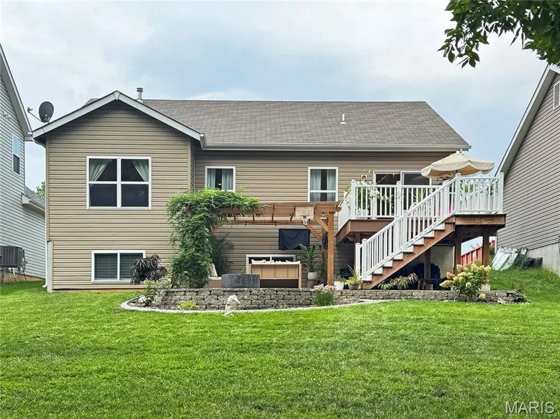 Expansive backyard with a manicured lawn, multi-level composite deck with white railings, and a wooden pergola structure — 4024 Glengarry Drive, Wentzville, MO 63385