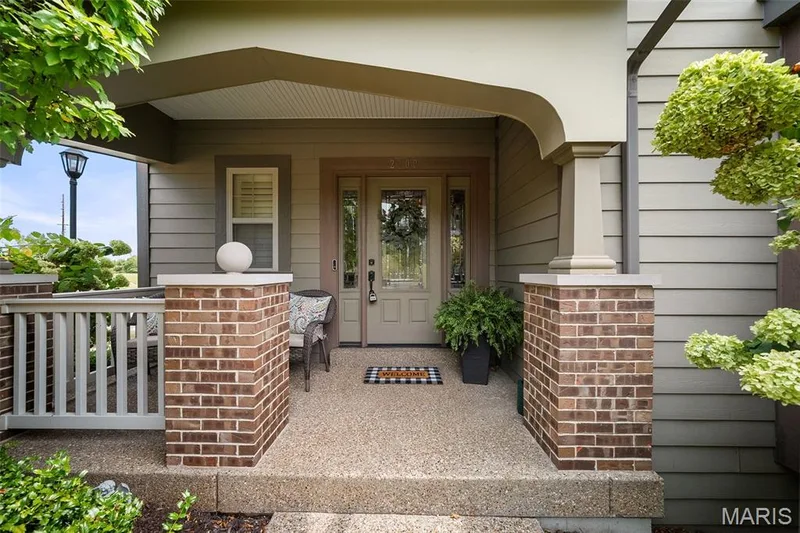 Inviting covered front porch with exposed aggregate concrete flooring, brick pillars, and horizontal siding — 2700 Grover Crossing Drive, Wildwood, MO 63040