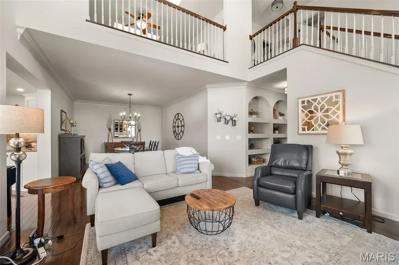 Two-story living area with dark wood-finish flooring, white spindle railings, and built-in shelving with arched accents — 2700 Grover Crossing Drive, Wildwood, MO 63040