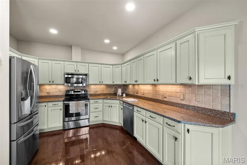 Kitchen featuring light-toned cabinetry, stainless steel appliances, speckled countertops, tile backsplash, and wood-finish flooring — 2700 Grover Crossing Drive, Wildwood, MO 63040