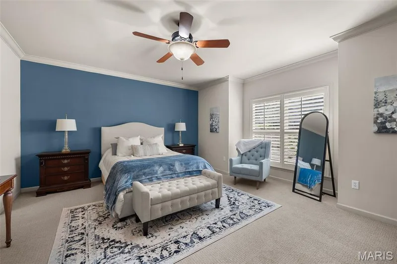 Neutral tone carpet flooring, crown molding, ceiling fan with light fixture, plantation shutters, and a prominent accent wall — 2700 Grover Crossing Drive, Wildwood, MO 63040