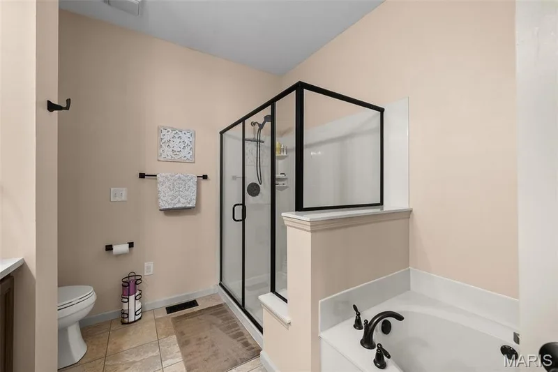 Tiled flooring leading to a glass-enclosed shower with black trim, a built-in bathtub with black fixtures, and a toilet — 2700 Grover Crossing Drive, Wildwood, MO 63040