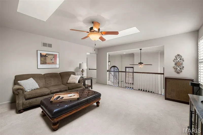 Carpeted loft area featuring a ceiling fan, two skylights, and a white railing overlooking the lower level — 2700 Grover Crossing Drive, Wildwood, MO 63040