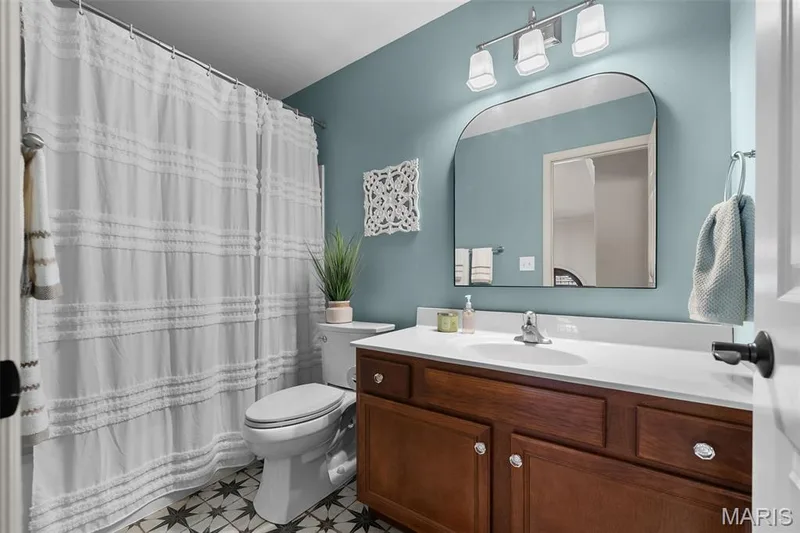 Bathroom featuring a wood vanity with a white countertop, patterned tile flooring, an arched mirror, and a three-light fixture — 2700 Grover Crossing Drive, Wildwood, MO 63040