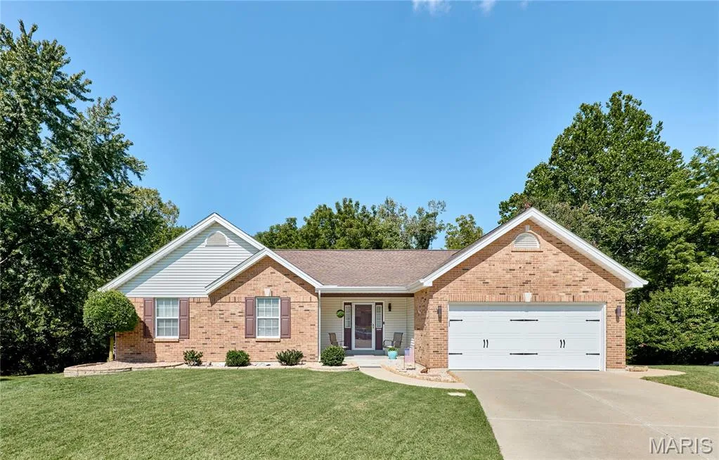Charming brick ranch home featuring a gabled roofline, welcoming front entrance with sidelights, manicured lawn with mature landscaping, and a two-car garage with white panel doors — 3641 Wind Chime Lane, St Charles, MO 63301
