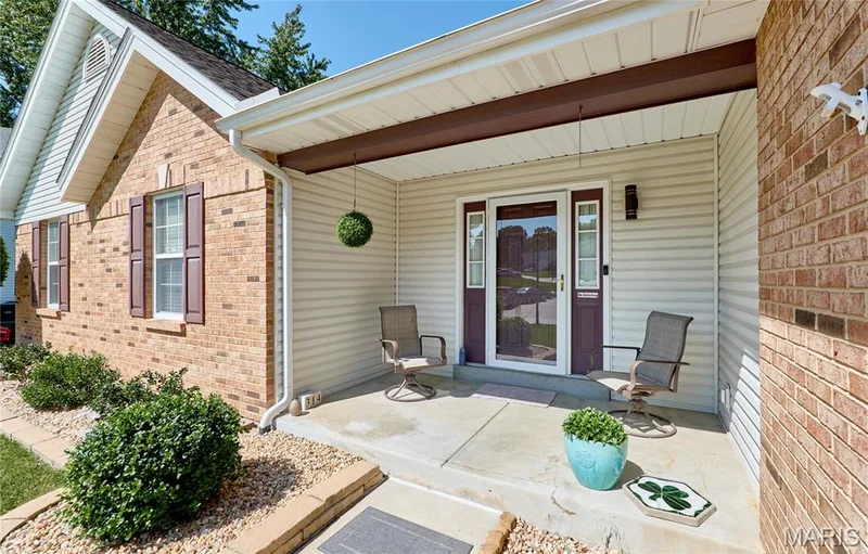 Welcoming front porch with a covered entryway featuring brick and vinyl siding exterior, dual French doors with glass panels, mature landscaping with boxwood shrubs, and concrete walkway — 3641 Wind Chime Lane, St Charles, MO 63301