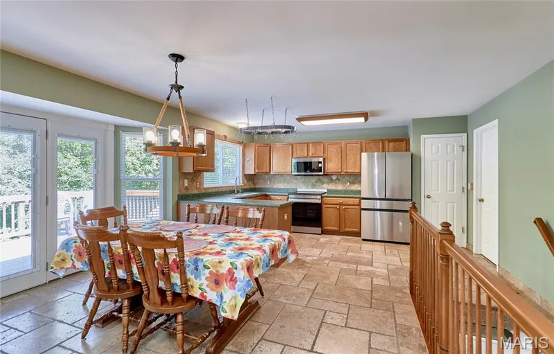 Open-concept kitchen and dining area featuring wood cabinetry, stainless steel appliances, tile flooring, and abundant natural light from multiple windows and glass doors accessing outdoor space — 3641 Wind Chime Lane, St Charles, MO 63301