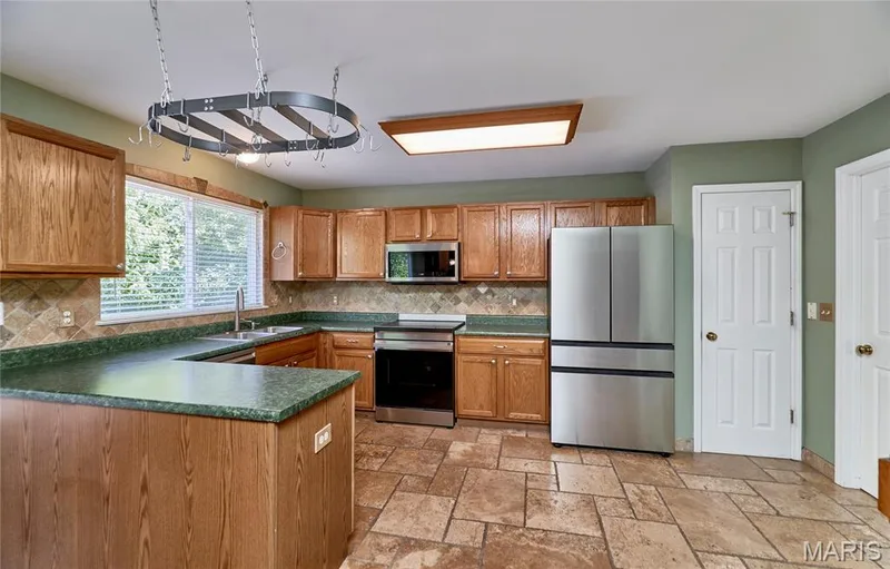 Spacious kitchen featuring wood cabinetry, stainless steel appliances, stone countertops, tile flooring, and a centered island with additional workspace — 3641 Wind Chime Lane, St Charles, MO 63301