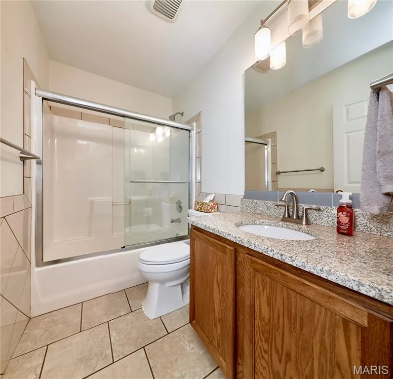 Spa-inspired bathroom featuring a wood-finish vanity with dual sinks, speckled stone countertops, and polished nickel fixtures — 3641 Wind Chime Lane, St Charles, MO 63301
