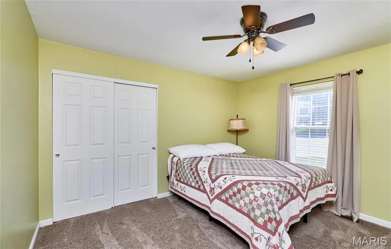 Bright secondary bedroom featuring soft yellow walls, carpet flooring, a ceiling fan with integrated lighting, and dual closet doors — 3641 Wind Chime Lane, St Charles, MO 63301