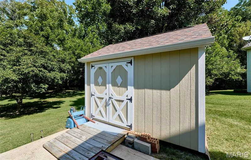Charming storage shed featuring dual barn-style doors with X-detailing, vertical wood siding, and a pitched roof with architectural shingles — 3641 Wind Chime Lane, St Charles, MO 63301