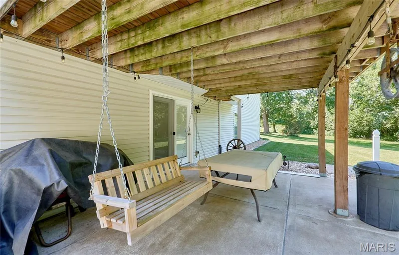 Covered patio with wood-beam ceiling and concrete flooring, featuring a suspended wood-slat swing — 3641 Wind Chime Lane, St Charles, MO 63301