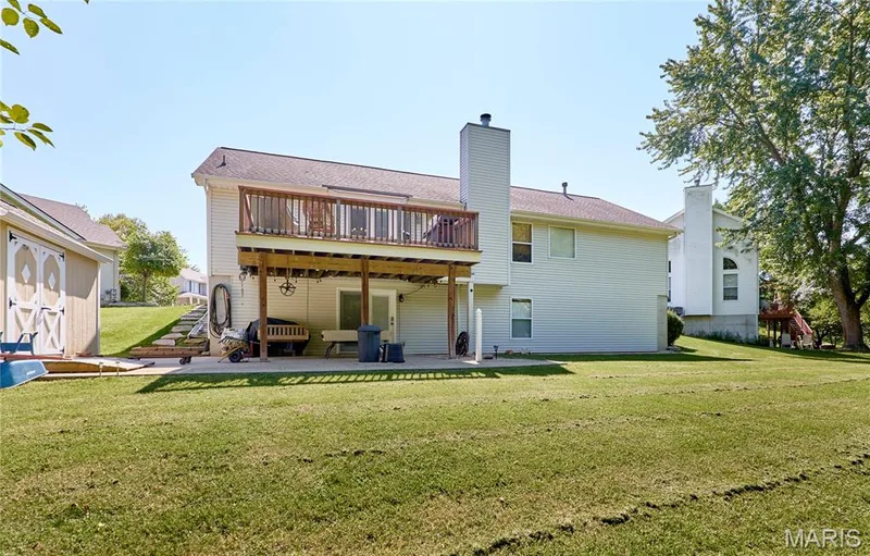 Expansive backyard featuring a manicured lawn, a raised wood deck with railing, a concrete patio, and an external storage shed — 3641 Wind Chime Lane, St Charles, MO 63301