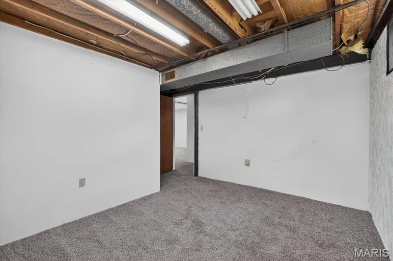 Carpeted room with exposed ceiling joists and ductwork, featuring fluorescent overhead lighting — 11 Toelle Drive, St Charles, MO 63304