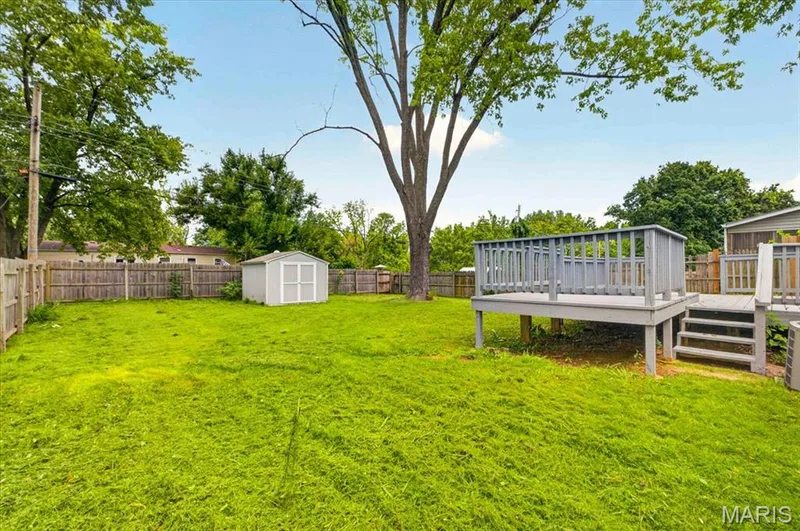 Expansive backyard featuring a wood privacy fence, a detached storage shed, a mature shade tree, and a raised wood deck with steps — 11 Toelle Drive, St Charles, MO 63304