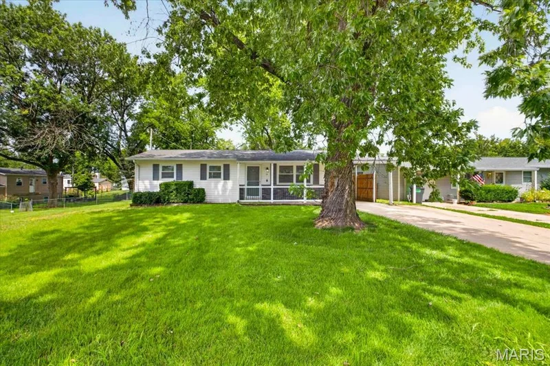 White exterior with dark shutters, front porch with screening, mature tree, and a concrete driveway — 11 Toelle Drive, St Charles, MO 63304