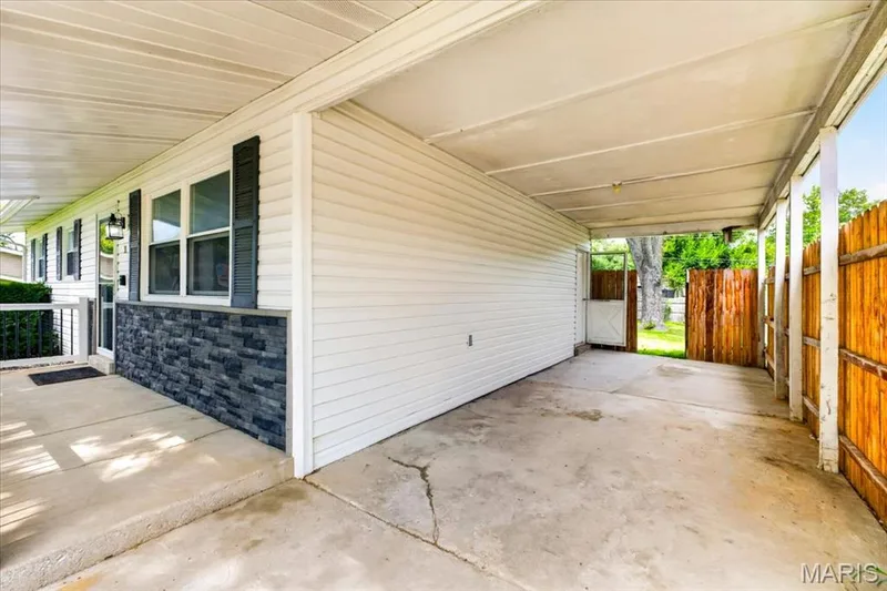 Covered carport with concrete flooring, accented by a wood privacy fence — 11 Toelle Drive, St Charles, MO 63304
