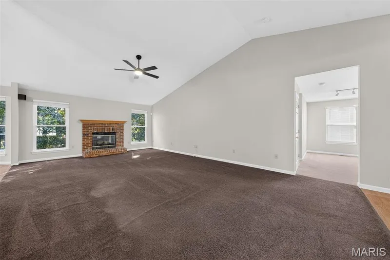 Vaulted ceiling with a ceiling fan, brick fireplace with a wood mantel, multiple windows, and carpet flooring — 155 Snake River Drive, Dardenne Prairie, MO 63368