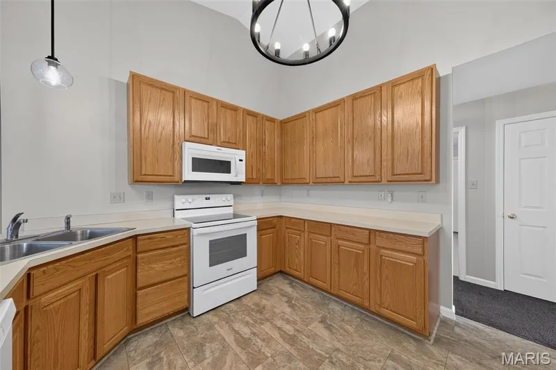 Kitchen featuring wood cabinetry, white appliances, a double basin stainless steel sink, and light-toned countertops — 155 Snake River Drive, Dardenne Prairie, MO 63368