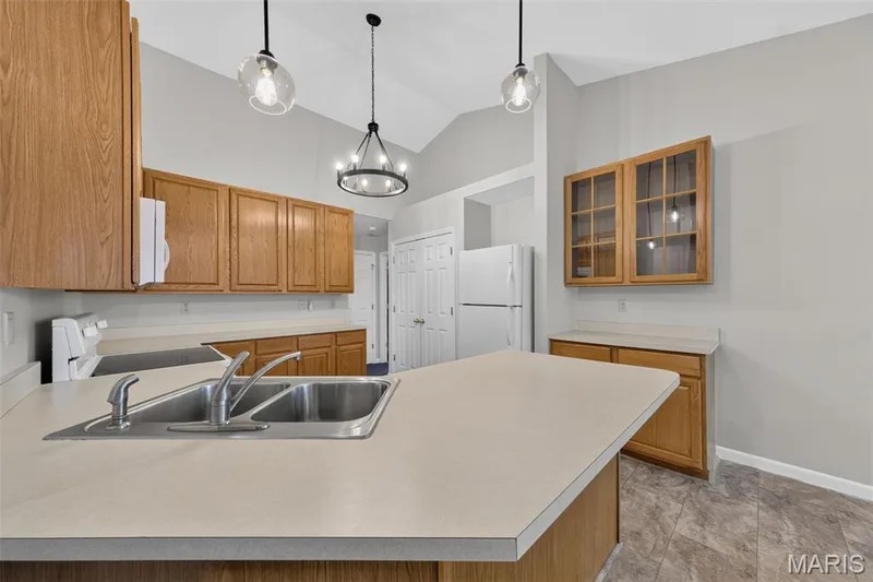 Kitchen featuring wood-finish cabinetry, solid surface countertops, a double basin stainless steel sink, and vaulted ceilings — 155 Snake River Drive, Dardenne Prairie, MO 63368