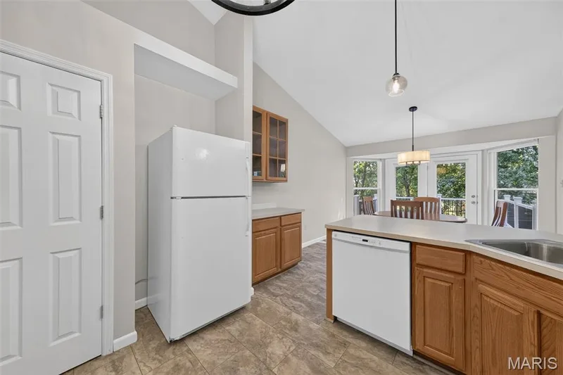 Vaulted ceiling kitchen featuring a built-in dishwasher, wood-finish cabinetry, and a stainless steel sink, with a dining area offering access to an outdoor deck — 155 Snake River Drive, Dardenne Prairie, MO 63368