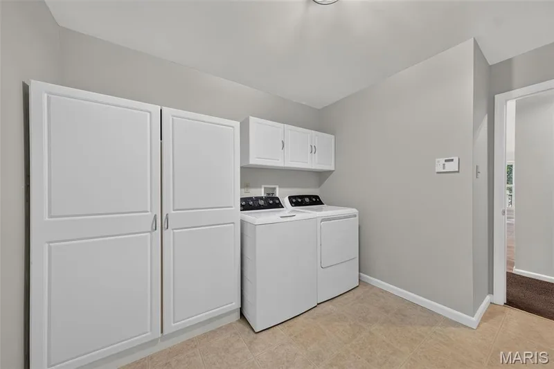 Laundry area featuring white cabinetry, overhead wall cabinets, ceramic tile flooring, and light gray wall paint — 155 Snake River Drive, Dardenne Prairie, MO 63368