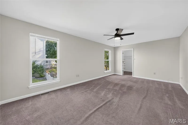 Spacious room with plush carpeting, two large windows, a ceiling fan with integrated lighting, and a walk-in closet with built-in shelving — 155 Snake River Drive, Dardenne Prairie, MO 63368