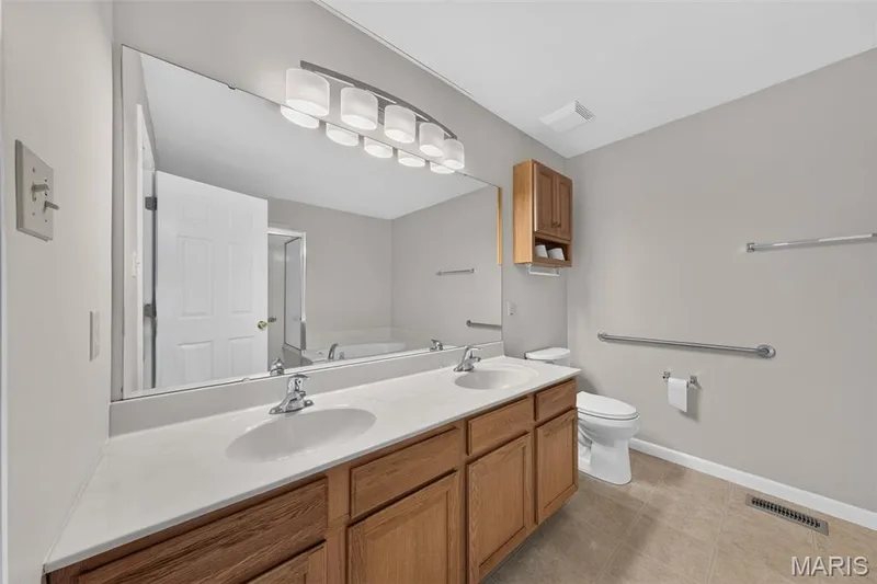 Dual vanity with integrated sinks, wood-finish cabinetry, and a large wall-mounted mirror — 155 Snake River Drive, Dardenne Prairie, MO 63368