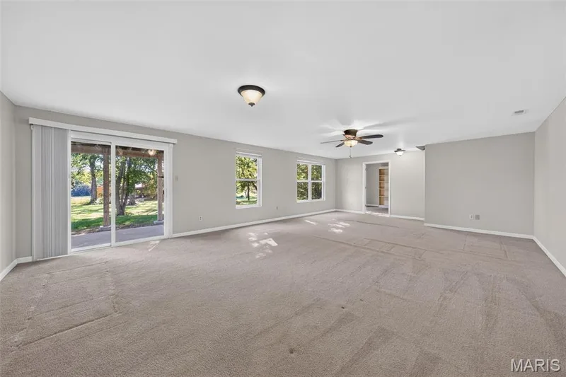 Spacious room with light gray walls, plush carpeting, multiple windows, a sliding glass door, and a ceiling fan — 155 Snake River Drive, Dardenne Prairie, MO 63368