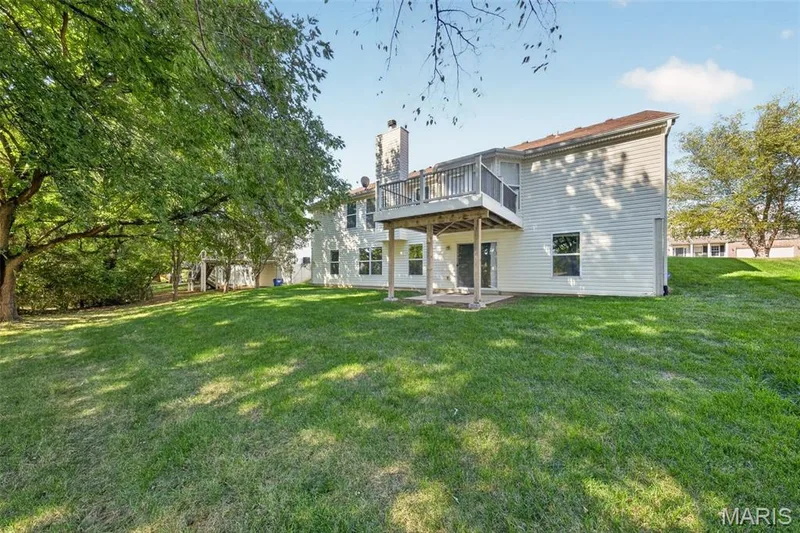 Expansive grassy yard with mature trees, a multi-level deck, and a lower-level concrete patio — 155 Snake River Drive, Dardenne Prairie, MO 63368