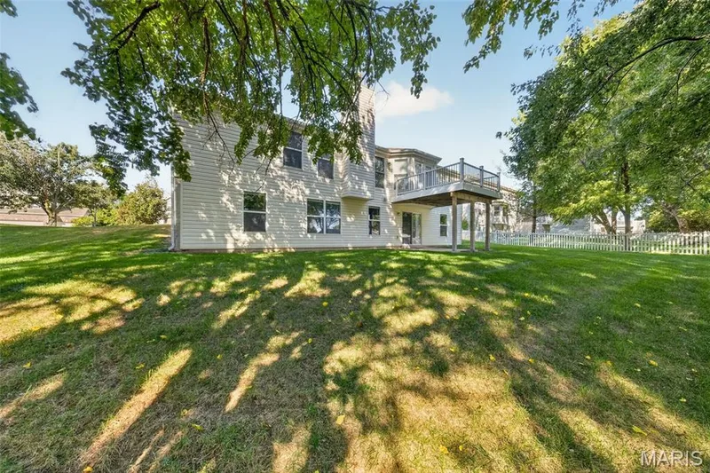 Expansive backyard with a manicured lawn, multi-level deck, white picket fencing, and mature trees — 155 Snake River Drive, Dardenne Prairie, MO 63368