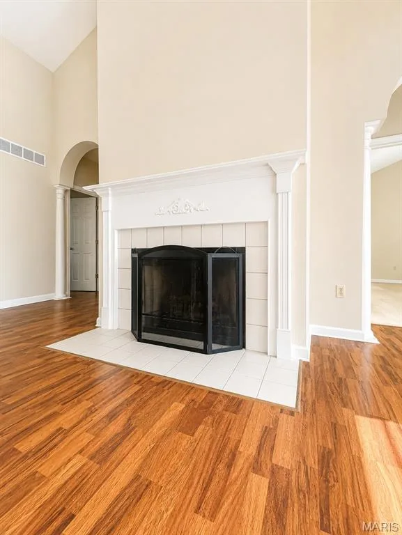 Elegant living space featuring a classic fireplace with white painted surround and black glass doors, gleaming wood-finish flooring throughout, soaring ceilings with architectural detail, arched entryway with trim work, and abundant natural light from multiple openings — 1605 Ridge Bend Drive, Glencoe, MO 63038