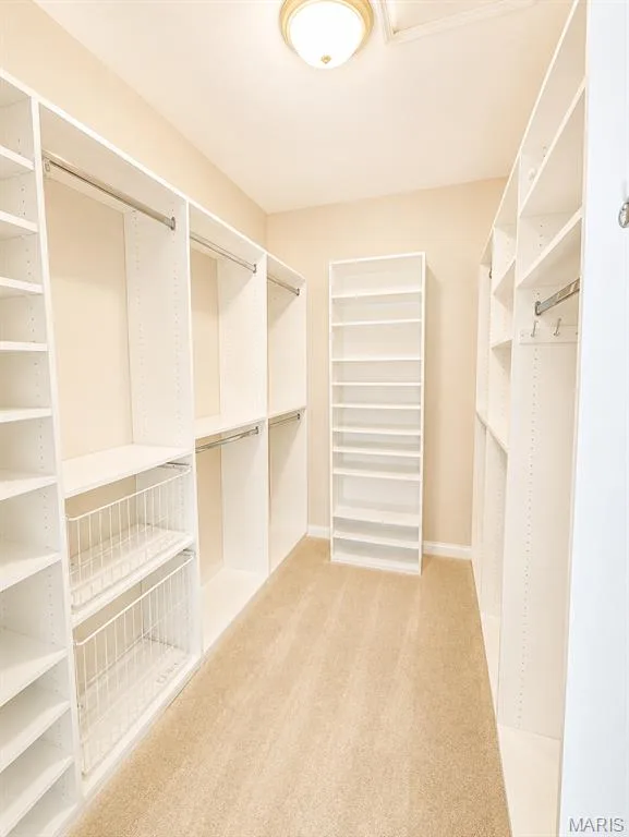 Spacious pimary walk-in closet featuring extensive white built-in shelving and hanging systems, wire storage baskets, wood-finish flooring, and recessed ceiling lighting throughout the organized storage space — 1605 Ridge Bend Drive, Glencoe, MO 63038