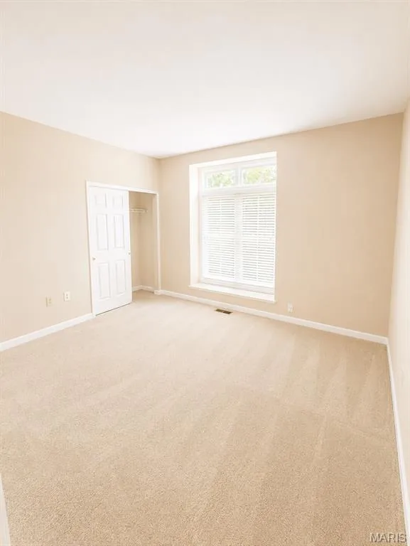Bright and spacious bedroom featuring neutral-toned walls, pristine carpeting, a large window with plantation shutters providing natural light, and a closet with bi-fold doors — 1605 Ridge Bend Drive, Glencoe, MO 63038