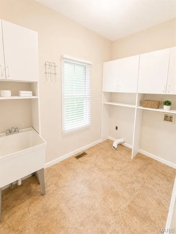 Bright utility room featuring white cabinetry with open shelving, a utility sink with chrome fixtures, cork-finish flooring, and abundant natural light from a horizontal sliding window with blinds — 1605 Ridge Bend Drive, Glencoe, MO 63038