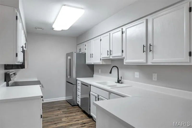 Kitchen featuring white cabinetry, light countertops, wood-finish flooring, stainless steel appliances, and a matte black faucet — 857 Du Pre Court, St Peters, MO 63376