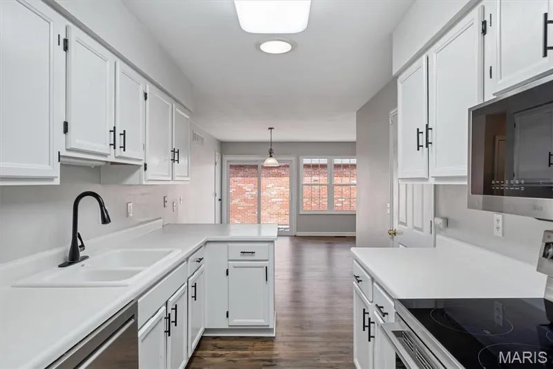 Galley kitchen featuring white cabinetry, light countertops, a dual-basin sink, and dark wood-finish flooring — 857 Du Pre Court, St Peters, MO 63376