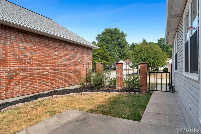 Brick exterior, concrete walkway, wrought iron gate with brick pillars, gray siding, and mature trees — 857 Du Pre Court, St Peters, MO 63376