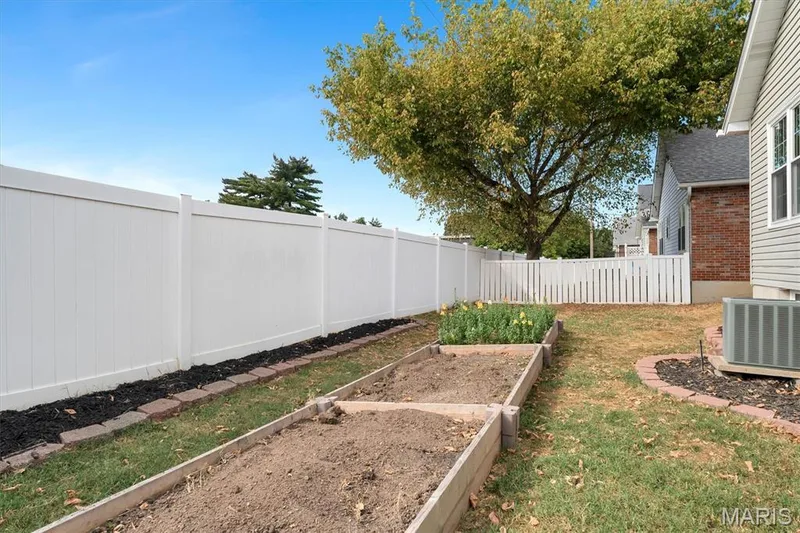 Enclosed backyard featuring a white privacy fence, raised garden beds, and a mature tree — 857 Du Pre Court, St Peters, MO 63376