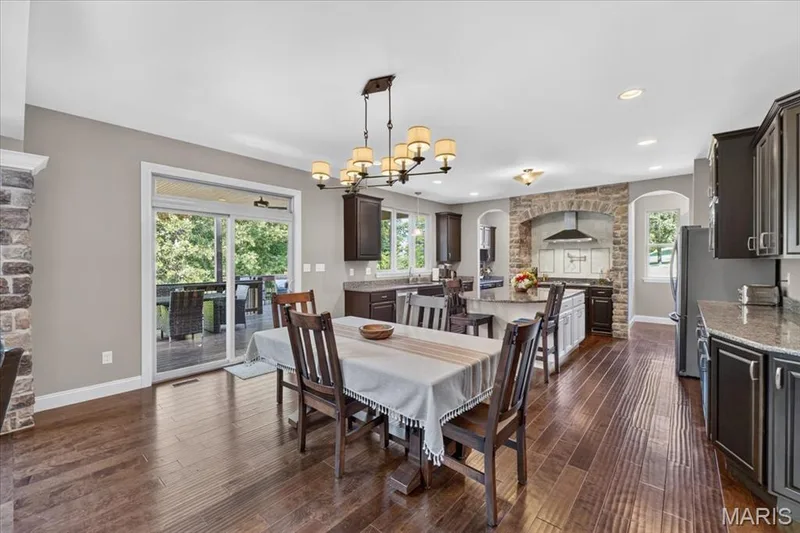 Open-concept living space featuring wood-finish flooring, a stone-accented archway, dark cabinetry, and a sliding glass door leading to the outdoor deck — 1307 Homestead Heights Drive, Wildwood, MO 63005