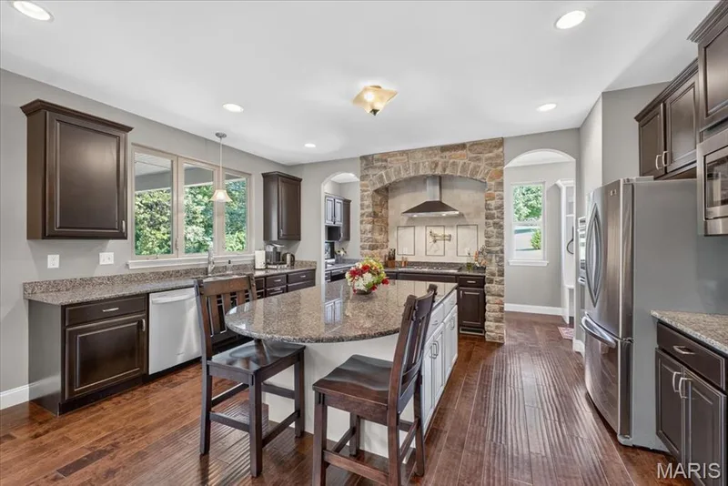 Kitchen featuring wood-finish flooring, dark cabinetry, granite countertops, and stainless steel appliances — 1307 Homestead Heights Drive, Wildwood, MO 63005